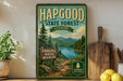 A vintage-style sign for Hapgood State Forest in Vermont, featuring a scenic landscape with pine trees, a lake, and mountains.