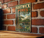 A vintage metal sign for Hartwick Pines State Park, featuring a scenic illustration of a forest and a bridge, mounted on a brick wall.