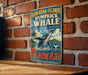 A vintage-style sign for the Hawaiian Islands humpback whale sanctuary, featuring a whale jumping out of the water and surrounded by tropical elements such as palm trees and flowers.