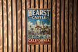 A vintage metal sign with the text "HEARST CASTLE CALIFORNIA" and an illustration of a castle surrounded by palm trees.