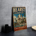 A vintage-style metal sign with the text "HEARST CASTLE CALIFORNIA" and an illustration of a castle, palm trees, and a fountain.