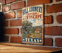 A vintage-style metal sign with the text "Hill Country Cultural Landscape" and "Texas" is displayed on a brick wall.