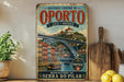 a vintage-style poster of the Luiz I Bridge in Portugal, displayed on a wall next to a wooden cutting board and some potted plants.