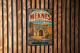 A vintage-style metal sign for the historic city of Meknes, Morocco, featuring an illustration of a palace or palace-like structure.