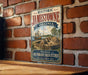 A vintage-style metal sign for Historic Jamestown, Virginia, featuring an illustration of a fort and ship, mounted on a brick wall.