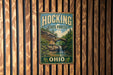 A vintage-style metal sign for Hocking State Forest in Ohio, featuring a scenic image of a waterfall and a bridge.