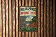 A vintage-style metal sign for Holly Springs National Forest in Mississippi, featuring a scenic image of the forest and a river.