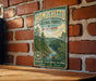 A vintage-style metal sign for the Homochito National Forest in Mississippi, featuring a scenic illustration of a forest landscape with a river.