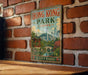 A vintage-style poster of Hong Kong Park, China, featuring a scenic illustration of the park and its surroundings, is displayed on a brick wall.