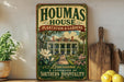 A vintage-style sign for "Houmas House Plantation & Gardens" in Louisiana, featuring a large illustration of a plantation house surrounded by lush greenery and flowers.