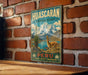 A vintage-style metal sign with a mountain landscape and a llama, mounted on a brick wall.