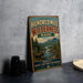 A vintage metal sign advertising " Hundred Mile Wilderness Maine" is displayed on a gray wall, with a wooden table and some items in the foreground.
