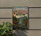 A vintage-style metal sign advertising " Hundred Mile Wilderness Maine" is displayed on a wall, featuring a scenic landscape with mountains, trees, and a moose.