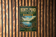 A vintage metal sign for the Hunts Pond State Forest in New York, featuring a scenic landscape with pine trees, a lake, and mountains.
