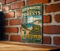 A vintage metal sign for Huron-Manistee National Forests, featuring a scenic image of a forest and a lake, mounted on a brick wall.