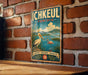 A vintage-style metal sign with the text "Ichkeul Tunisia" and a scenic illustration of a heron and flamingos in a lake, set against a brick wall.