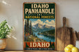 A vintage-style metal sign advertising the Idaho Panhandle National Forests, featuring a scenic mountain landscape with pine trees and a lake.