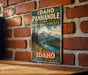 A vintage-style metal sign for Idaho Panhandle National Forests, featuring a scenic mountain landscape with pine trees and a lake.