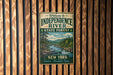 A vintage-style metal sign that reads "Welcome to Independence River State Forest New York Explore Discover Enjoy" is displayed on a wooden wall.