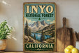 A vintage-style metal sign for Inyo National Forest in California, featuring a scenic mountain landscape with pine trees and a lake.