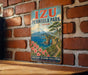 A vintage-style metal sign for Izu Peninsula Park in Japan, featuring a scenic landscape with mountains, a river, and a path leading through the natural setting.
