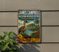 A vintage-style metal sign with a bird illustration and tropical landscape, mounted on a wall next to a plant.