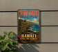 A vintage-style metal sign advertising the "Ka'u Coast Cultural Landscape" in Hawaii, featuring a tiki statue and a tropical landscape.