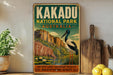 A vintage-style metal sign for Kakadu National Park in Australia, featuring an illustration of a bird and a landscape with water and flowers.