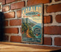 A vintage-style metal sign with the text "KALALAU TRAIL" and "Kauai, Hawaii" is displayed on a brick wall.