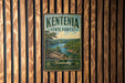 A vintage metal sign for Kentonia State Forest hangs on a wooden wall, featuring a scenic landscape with a lake and mountains.