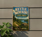 A vintage metal sign for Kettle Moraine State Forest in Wisconsin, featuring a scenic landscape with a river, mountains, and pine trees.