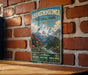 A vintage-style metal sign for Khangchenzonga National Park in India, featuring a mountain landscape with flowers and a river.