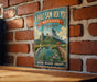 A vintage-style metal sign with a scenic illustration of a lake, mountains, and a bird, mounted on a brick wall.