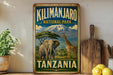 A vintage-style sign for Kilimanjaro National Park in Tanzania, featuring an elephant and a giraffe in a lush, green landscape with a snow-capped mountain in the background.