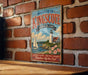 A vintage-style metal sign that reads "Welcome to Kingscote, Rhode Island" with a lighthouse and sailboat illustration, mounted on a brick wall.