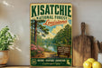 A vintage-style sign for the Kisatchie National Forest in Louisiana, featuring a scenic landscape with a river, pine trees, and flowers.