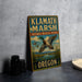 A vintage-style sign for Klath Marsh National Wildlife Refuge in Oregon, featuring a duck in flight and surrounded by tall grasses.