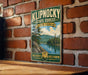 A vintage-style metal sign for the Klipnocky State Forest in New York, featuring a scenic landscape with pine trees, a lake, and mountains.
