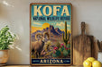 A vintage-style metal sign for the Kofa National Wildlife Refuge in Arizona, featuring a mountain landscape with a goat and cactus in the foreground.