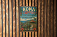 A vintage Kona Coffee sign is displayed on a wooden wall, featuring a tropical landscape with a house, palm trees, and coffee plants.