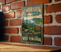 A vintage-style metal sign for the Kumbarow State Forest in West Virginia, featuring a scenic landscape with a river and mountains.