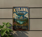 A vintage-style metal sign for Kuskawa Territorial Park in Yukon, Canada, featuring a scenic mountain landscape with a lake and pine trees.