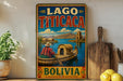A vintage-style sign for "Lago Titicaca" in Bolivia, featuring a woman in a canoe on a river surrounded by mountains and buildings.