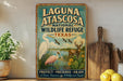 A vintage-style sign for Laguna Atascosa National Wildlife Refuge in Texas, featuring illustrations of wildlife such as a crane, deer, and cactus.