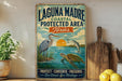 A vintage-style metal sign for the Laguna Madre Coastal Protected Area in Texas, featuring illustrations of a heron, a fish, and a turtle in a serene coastal landscape.