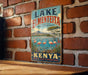A vintage-style sign for Lake Elmenteita, the bird-watching destination in Kenya, featuring a scenic landscape with flamingos and palm trees.