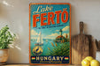 A vintage-style sign for Lake Fertö, the jewel of Western Hungary, featuring a sailboat and a lighthouse, is displayed on a shelf next to a wooden cutting board and some lemons.