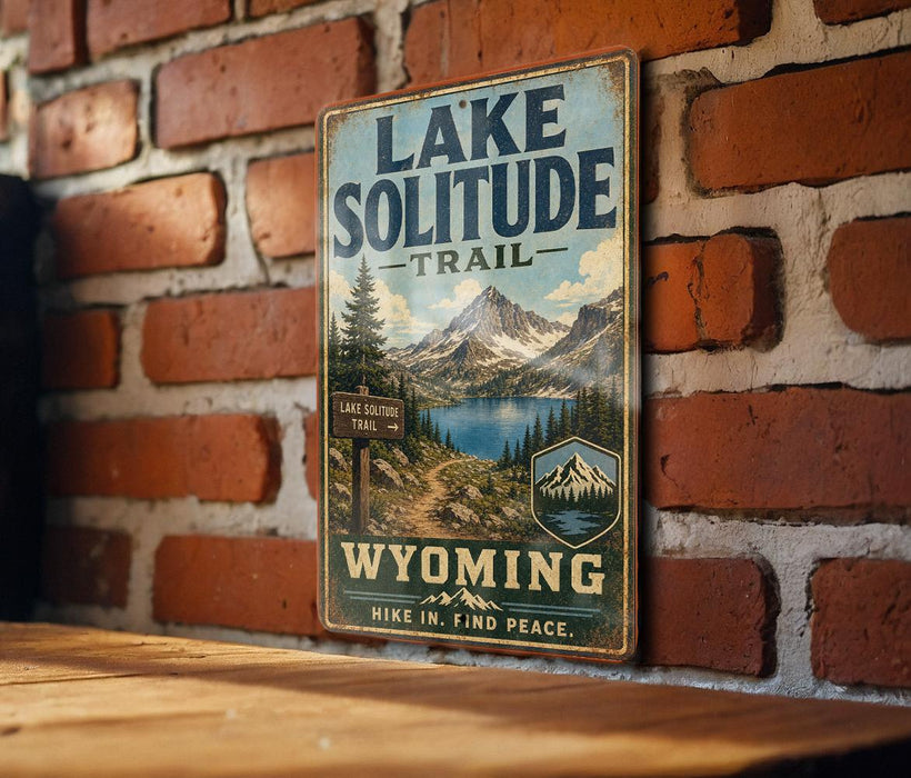 A vintage-style metal sign for the Lake Solitude Trail in Wyoming, featuring a scenic mountain landscape and a trail sign.