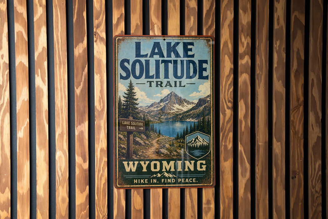 A vintage-style metal sign for the Lake Solitude Trail in Wyoming, featuring a scenic mountain landscape and a trail sign.