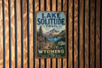 A vintage-style metal sign for the Lake Solitude Trail in Wyoming, featuring a scenic mountain landscape and a trail sign.